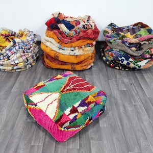 May include: Four colorful Moroccan poufs and floor cushions. The poufs are in various shapes and sizes, with vibrant geometric patterns in shades of pink, green, red, and blue. The floor cushions are round and stacked.