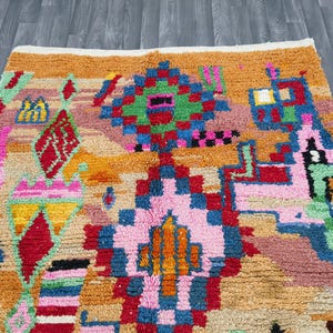 May include: A colorful, patterned rug with a geometric design. The rug features a variety of colors, including orange, pink, green, blue, and red. The design includes diamond and square shapes.