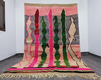 May include: A colorful, handmade rug with a geometric design. The rug features vertical stripes in shades of pink, green, gray, and beige. The rug has a fringed edge and is made of a thick, woven material.