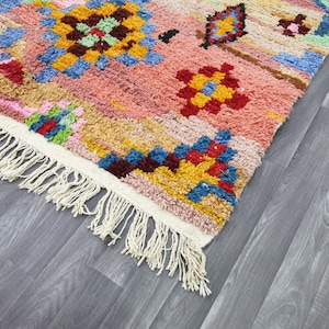May include: A colorful, patterned rug with a pink, yellow, blue, and red design. The rug has a white fringe along one edge. The rug's design features geometric shapes and floral patterns.