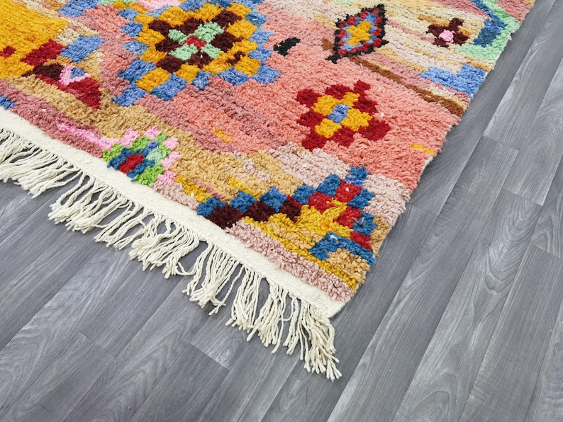 May include: A colorful, patterned rug with a pink, yellow, blue, and red design. The rug has a white fringe along one edge. The rug's design features geometric shapes and floral patterns.