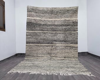 May include: A large, rectangular rug with a geometric pattern. The rug features a gradient of gray tones, with white accents and a fringed edge. The design includes diamond shapes and horizontal stripes.