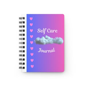 May include: A spiral-bound notebook with a blue to pink gradient cover. The front features a vertical row of small pink hearts on the left, a central white cloud graphic, and the white text "Self Care Journal" printed above and below the cloud.
