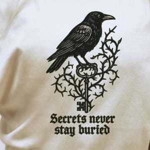 Camiseta de cuervo "Secrets Never Stay Buried" / Camiseta gótica de misterio con colores cómodos para lectores amantes de los libros, camiseta de cuervo de la academia oscura, corte relajado unisex