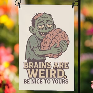 Puede incluir: Una bandera de jardín con un zombi de dibujos animados sosteniendo un cerebro. El zombi es verde con una camisa rasgada y una sonrisa tonta. La bandera tiene el texto "BRAINS ARE WEIRD, BE NICE TO YOURS" en marrón y blanco.