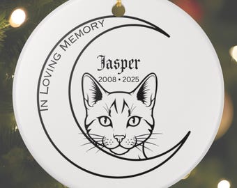 May include: A white ceramic ornament with a gold string for hanging. The ornament features a black and white cat face inside a crescent moon. Text reads "IN LOVING MEMORY" and "Jasper 2008-2025".