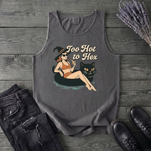 May include: A charcoal grey sleeveless tank top featuring a graphic print of a person in a witch hat and bikini lounging on a black cat-shaped pool float while holding a cocktail. The text Too Hot to Hex is printed above the illustration.