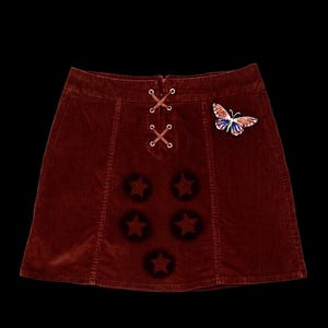 Minifalda vintage de pana marrón con cintura con cordones, parches de estrellas y detalle de mariposa.
