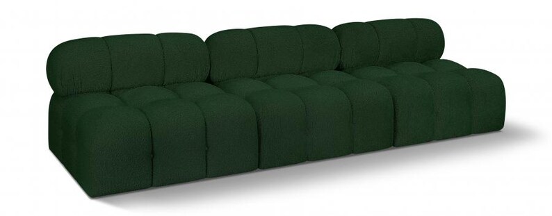 K&ouml;nnte beinhalten: Ein dunkelgr&uuml;nes, modulares Sofa mit niedrigem Profil. Das Sofa besteht aus drei verbundenen Teilen, jedes mit einem getufteten, kastenf&ouml;rmigen Design. Die Kissen und R&uuml;ckenlehnen sind abgerundet und wirken einladend. Das Sofa steht direkt auf dem Boden.
