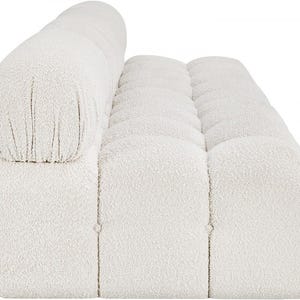K&ouml;nnte beinhalten: Ein cremefarbenes, modernes Sofa mit abgerundeter R&uuml;ckenlehne und getufteter Sitzfl&auml;che. Das Sofa hat einen strukturierten Boucl&eacute;-Stoff und ein niedriges Profil. Das Design zeigt eine Reihe quadratischer Kissen und ein zylindrisches Kissen f&uuml;r den R&uuml;cken.