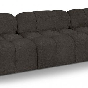 K&ouml;nnte beinhalten: Ein dunkelbraunes Dreisitzer-Sofa mit getuftetem Design. Das Sofa hat ein niedriges Profil und eine abgerundete R&uuml;ckenlehne. Die Kissen sind quadratisch und gleichm&auml;&szlig;ig verteilt. Das Sofa ist aus einem strukturierten Stoff gefertigt.