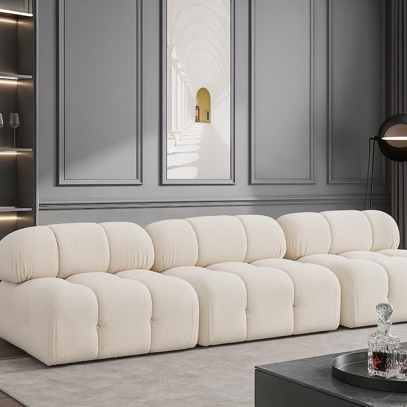 K&ouml;nnte beinhalten: Ein cremefarbenes, modulares Sofa mit einem abgerundeten, getufteten Design. Das Sofa besteht aus mehreren Einzelteilen und schafft eine weiche und einladende Sitzanordnung. Die neutrale Farbe und das moderne Design machen es zu einem vielseitigen M&ouml;belst&uuml;ck.