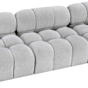 K&ouml;nnte beinhalten: Ein hellgraues, modulares Sofa mit einem abgerundeten, strukturierten Design. Das Sofa verf&uuml;gt &uuml;ber eine Reihe einzelner, gepolsterter Abschnitte, die ein einzigartiges, wolkenartiges Aussehen erzeugen. Die R&uuml;ckenlehne besteht aus drei rechteckigen Abschnitten, und der Sitz hat mehrere abgerundete Abschnitte.