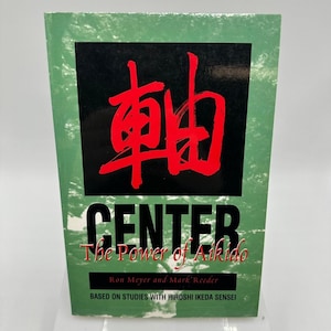 May include: A green book cover with a black rectangle featuring large red Japanese characters. Below, the word "CENTER" is in large white letters, with "The Power of Aikido" beneath it. The authors' names and a statement about studies are at the bottom.