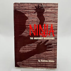 May include: A book cover featuring the title "NINJA" in red, set against a bamboo-style background. The subtitle reads "THE INVISIBLE ASSASSINS", with the author's name, Andrew Adams, at the bottom. A ninja silhouette is also visible.