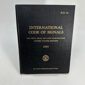 Może przedstawiać: Czarna książka w twardej oprawie zatytułowana International Code of Signals for Visual, Sound, and Radio Communications, United States Edition, 1969. Okładka zawiera złoty tekst, oznaczenie H.O. 102 oraz pieczęć U.S. Naval Oceanographic Office.
