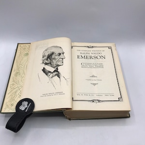 Może przedstawiać: Otwarta książka zatytułowana "The Complete Writings of Ralph Waldo Emerson" z portretem Emersona. Książka jest oprawiona w ciemną okładkę i zawiera czarny skórzany zakładkę. Tekst na okładce brzmi "WM. H. Wise & Co. Publishers New York."
