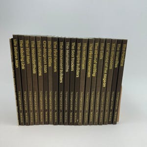 Puede incluir: Una colección de libros de tapa dura marrones de la serie "The Emergence of Man". Los títulos incluyen "Life Before Man", "The Missing Link" y "The Persians". Los libros están apilados sobre una superficie blanca.