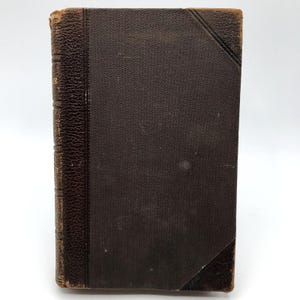 May include: A dark brown leather-bound book with a textured spine and gold lettering. The book is closed and appears to be old.