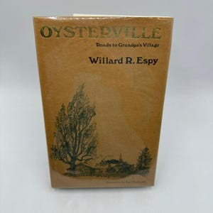 May include: A hardcover book titled "Oysterville Roads to Grandpa's Village" by Willard R. Espy. The cover is a light brown with gold lettering and a black and white illustration of a tree and a village.