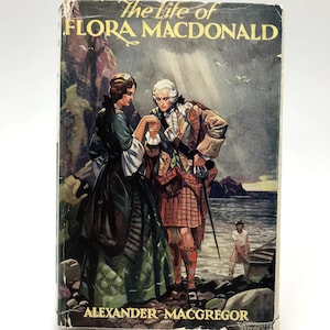 May include: The Life of Flora Macdonald book cover featuring a painting of a couple in traditional Scottish clothing standing on a rocky beach. The man is wearing a kilt and the woman is wearing a long dress. The title "The Life of Flora Macdonald" is printed in gold lettering on the cover.