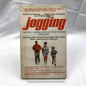 May include: A book cover with the title "jogging" in red letters. The cover features a photo of three people jogging, two adults and a child. The book is a medically approved physical fitness program for all ages, prepared by a heart specialist and a famous track coach. The book cover includes quotes from the U.S. Secretary of the Interior, The New York Times, and Life Magazine.