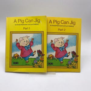 Può includere: Due libri per bambini vintage intitolati "A Pig Can Jig" di Donald Rasmussen e Lynn Goldberg. Vengono visualizzate le parti 1 e 2. Le copertine sono gialle con un'illustrazione di maiale dei cartoni animati.