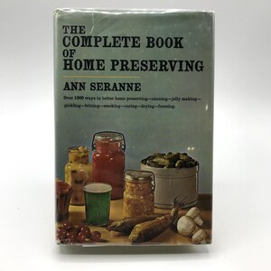 Könnte beinhalten: Ein Vintage-Buch mit dem Titel "The Complete Book of Home Preserving" von Ann Seranne. Das Cover zeigt einen blaugrünen Hintergrund mit Bildern von konservierten Lebensmitteln in Gläsern und Behältern, darunter Gurken, Tomaten und Mais. Das Buch verspricht über 1000 Möglichkeiten zur besseren Konservierung zu Hause.