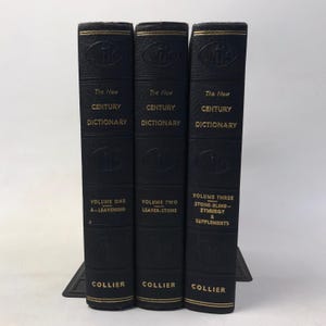 Könnte beinhalten: Drei schwarze Hardcover-Bücher mit dem Titel "The New Century Dictionary" mit goldener Schrift. Die Buchrücken zeigen die Bandnummer und den Verlag Collier. Die Bücher stehen auf einem schwarzen Buchstützen.