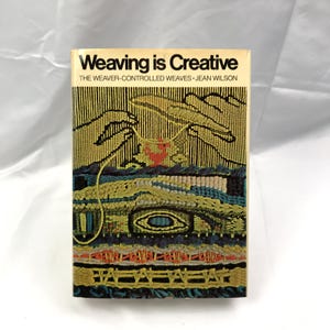 Może przedstawiać: Zabytkowa książka zatytułowana "Weaving is Creative" z kolorowym, tkanym wzorem na okładce. Okładka przedstawia dłonie tkające, z tekstem "THE WEAVER-CONTROLLED WEAVES JEAN WILSON". Książka ma kremowe tło.