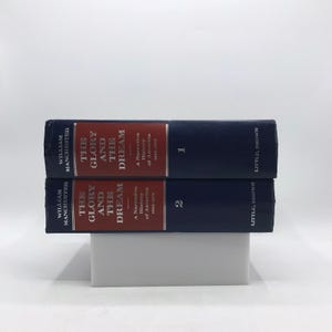 Peut inclure: Deux livres reliés, intitulés "The Glory and the Dream: A Narrative History of America 1932-1972" par William Manchester. Les livres sont bleu foncé avec du texte rouge et blanc. Le livre du haut est numéroté "1" et le livre du bas "2".