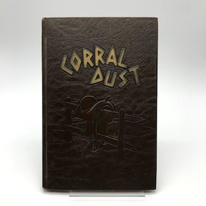 May include: A vintage brown book titled "Corral Dust" with embossed lettering and a western-themed illustration. The cover features a saddle and fence design, suggesting a theme related to the American West.