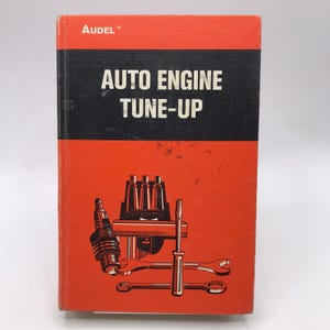 Puede incluir: Un libro antiguo titulado "AUTO ENGINE TUNE-UP" de Audel. La portada es roja y negra, con ilustraciones de componentes de motor y herramientas. El libro parece ser una guía para el mantenimiento automotriz.