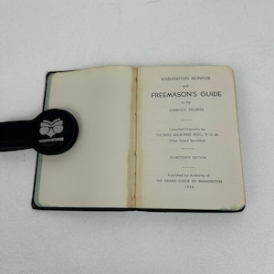 Könnte beinhalten: Ein aufgeschlagenes Buch mit dem Titel Washington Monitor and Freemason's Guide to the Symbolic Degrees, vierzehnte Ausgabe, veröffentlicht 1956 von der Grand Lodge of Washington. Ein schwarzer runder Clip mit Eulenlogo ist links befestigt.