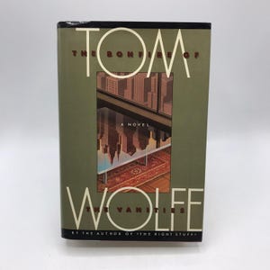 Puede incluir: Un libro de tapa dura titulado "La hoguera de las vanidades" de Tom Wolfe. La portada presenta un paisaje urbano reflejado en una ventana, con el nombre del autor y el título en letras blancas sobre un fondo verde.