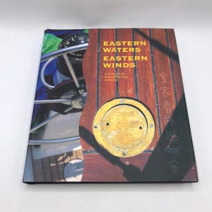 May include: A hardcover book titled "Eastern Waters Eastern Winds" with a wooden boat deck design. The cover features a compass, a brass plate, and text in English and Chinese. The book is a history of the Royal Hong Kong Yacht Club.