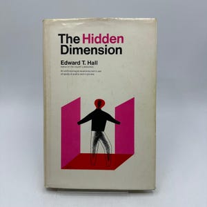 Może przedstawiać: Zabytkowa książka zatytułowana "The Hidden Dimension" autorstwa Edwarda T. Halla. Okładka przedstawia grafikę osoby w różowo-czerwonym geometrycznym wzorze. Tytuł książki jest w kolorze czarnym i różowym.