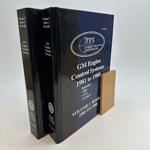 May include: Two black hardbound technical manuals titled GM Engine Control Systems 1981 to 1988 by Target Training Systems, Inc. The covers feature white text, a blue oval logo, and list DFI, CCC, and CLECS. The books are supported by a light wood bookend.