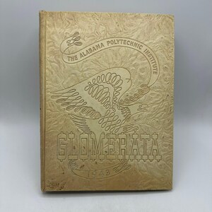 May include: Tan-colored hardcover book with embossed text and design. The cover features an eagle and the words "THE ALABAMA POLYTECHNIC INSTITUTE" and "GLOMERATA 1943". The book has a textured surface.