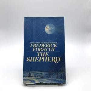 May include: A vintage hardcover book titled "The Shepherd" by Frederick Forsyth. The cover features a dark blue background with a full moon, an airplane, and a winter landscape. The title and author's name are in white.