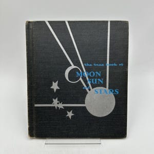 May include: A vintage book titled "The True Book of Moon, Sun and Stars." The cover is dark blue with white and light blue graphics of celestial bodies and lines. The book has a worn appearance.