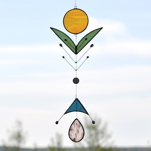 Pode incluir: Um m&oacute;bile de vidro colorido com um c&iacute;rculo amarelo, folhas verdes, um tri&acirc;ngulo azul e uma l&aacute;grima rosa.