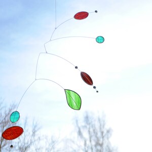 May include: A mobile made of glass and wire with red, green, and blue pieces. The mobile is hanging from the ceiling and is suspended in mid-air.