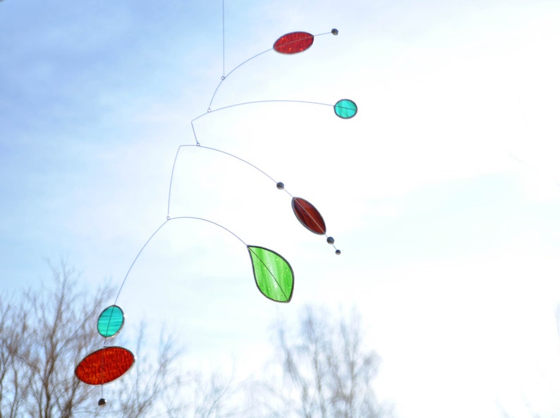 May include: A mobile made of glass and wire with red, green, and blue pieces. The mobile is hanging from the ceiling and is suspended in mid-air.
