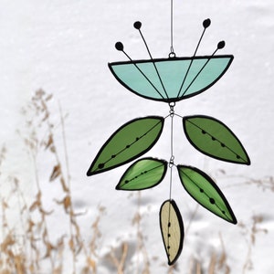 May include: A stained glass suncatcher featuring a blue flower and green leaves. The suncatcher is suspended from a wire.