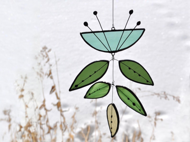 May include: A stained glass suncatcher featuring a blue flower and green leaves. The suncatcher is suspended from a wire.