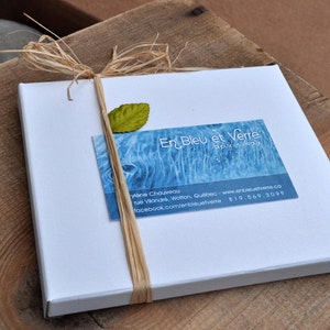 May include: A white box with a blue and white business card that says "En Bleu et Verre" and includes contact information. The box is tied with a natural twine bow and a green leaf is attached to the twine.
