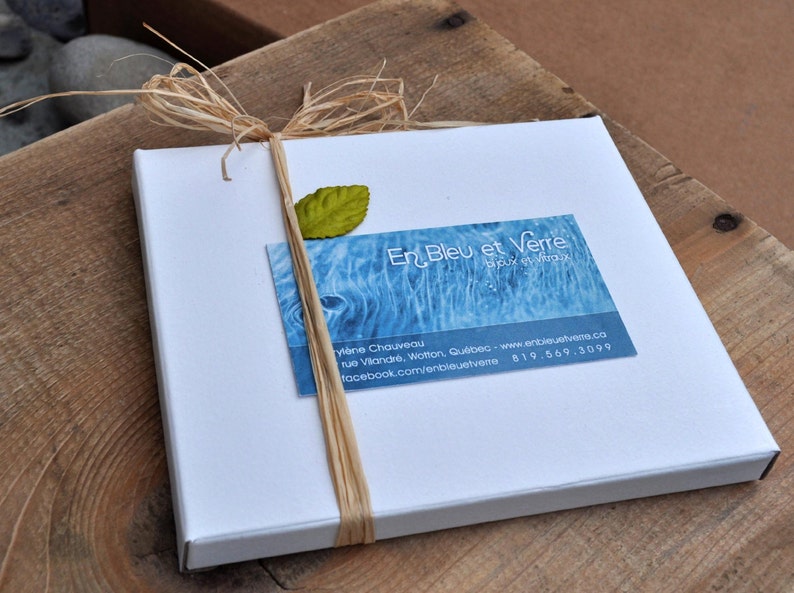May include: A white box with a blue and white business card that says "En Bleu et Verre" and includes contact information. The box is tied with a natural twine bow and a green leaf is attached to the twine.