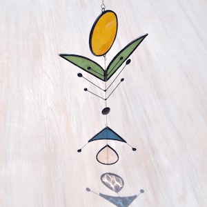 Pode incluir: Um m&oacute;bile de vidro colorido com um c&iacute;rculo amarelo, folhas verdes e formas geom&eacute;tricas azuis e brancas.