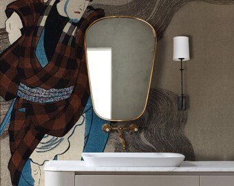 May include: A bathroom vanity featuring a gold-framed mirror, a white sink, and a wall-mounted lamp. The wall displays a large mural of a Japanese figure in a plaid robe. The vanity is a light grey colour.